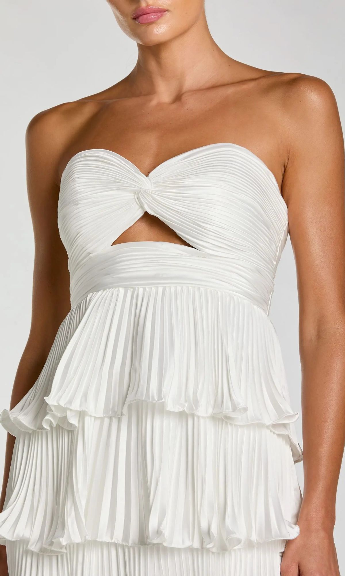 Woman wearing the Mac Duggal 49981 long formal dress, a strapless white gown with a knotted bodice, small front cutout, and layered pleated skirt.